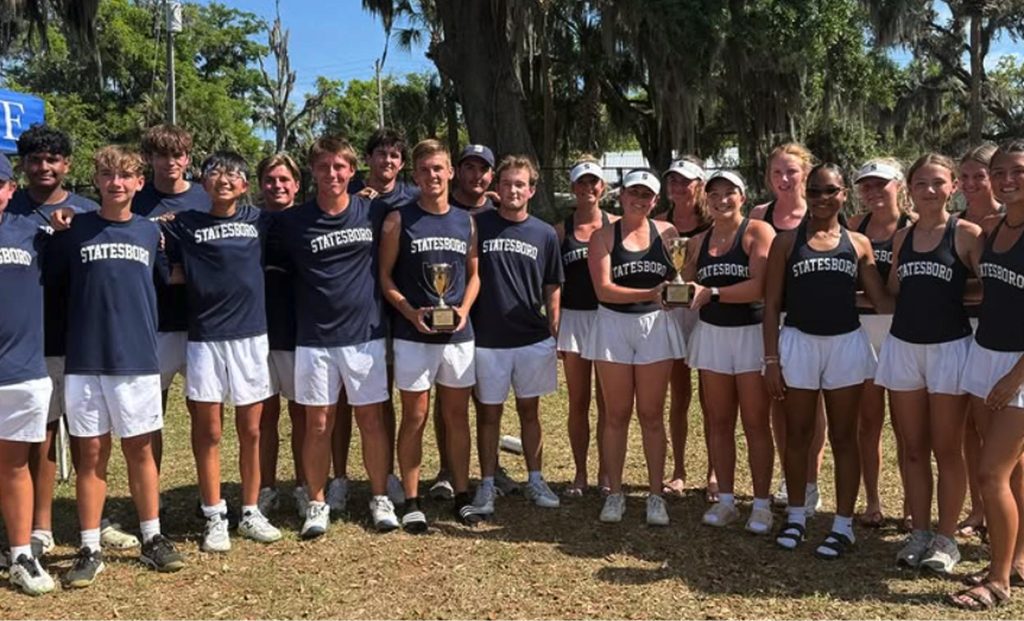 A group of young men and women in matching “Statesboro” athletic outfits pose outdoors, some holding trophies, smiling under trees draped with Spanish moss.