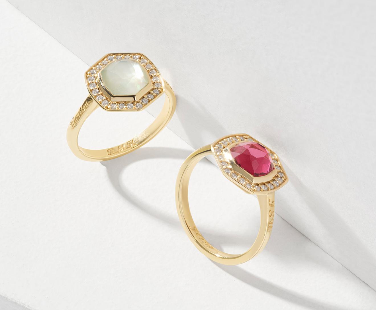 Two gold rings with hexagonal gemstone settings are displayed; one features a pale green gem, the other a pink gem, both surrounded by small diamonds, set against a white, angled background.