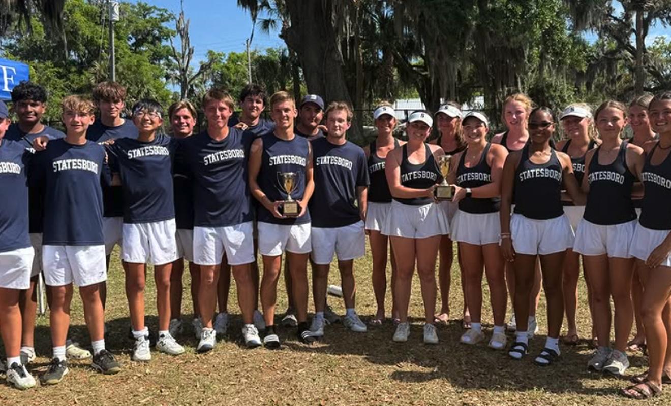 A group of young men and women in matching “Statesboro” athletic outfits pose outdoors, some holding trophies, smiling under trees draped with Spanish moss.
